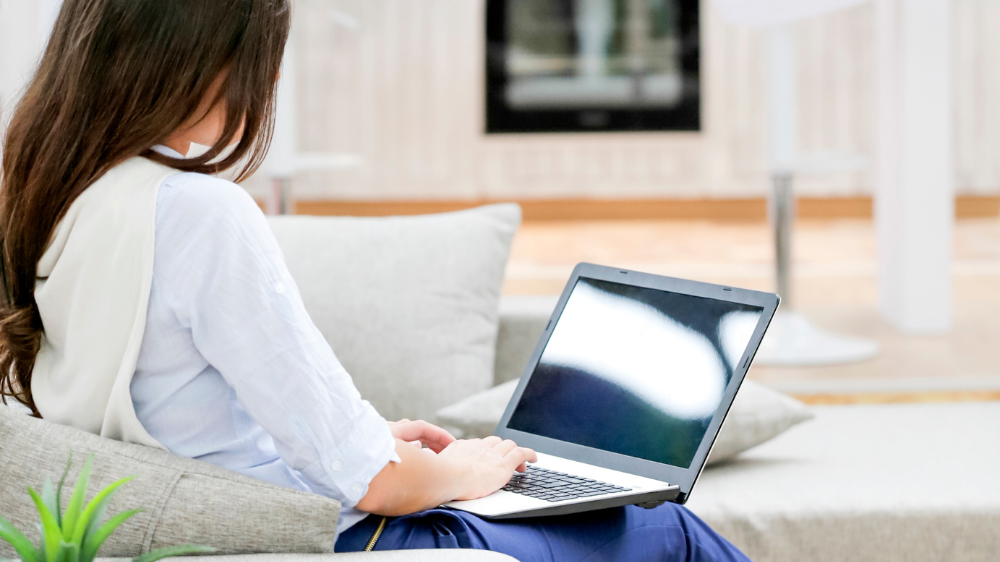 A writer writing nursing blogs on laptop, sitting on sofa, rear view