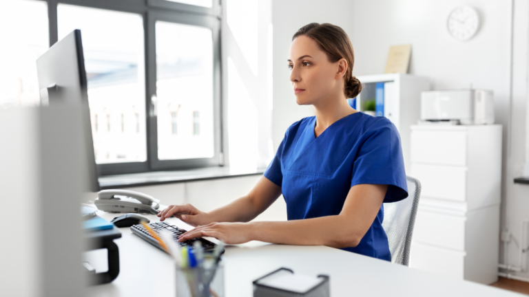 a nurse writer wearing a blue uniform working on her computer