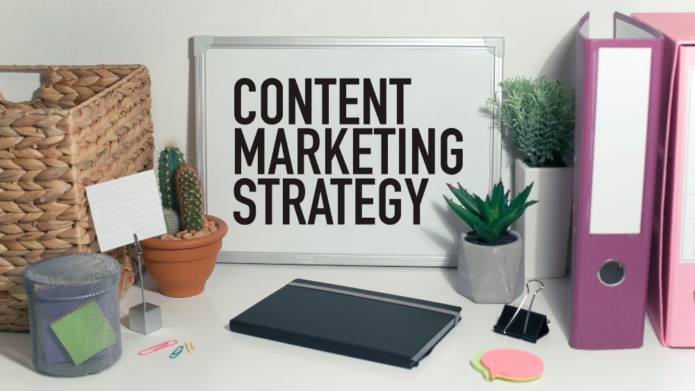 A desk with office supplies and a white board with words written, "content marketing strategy" on it