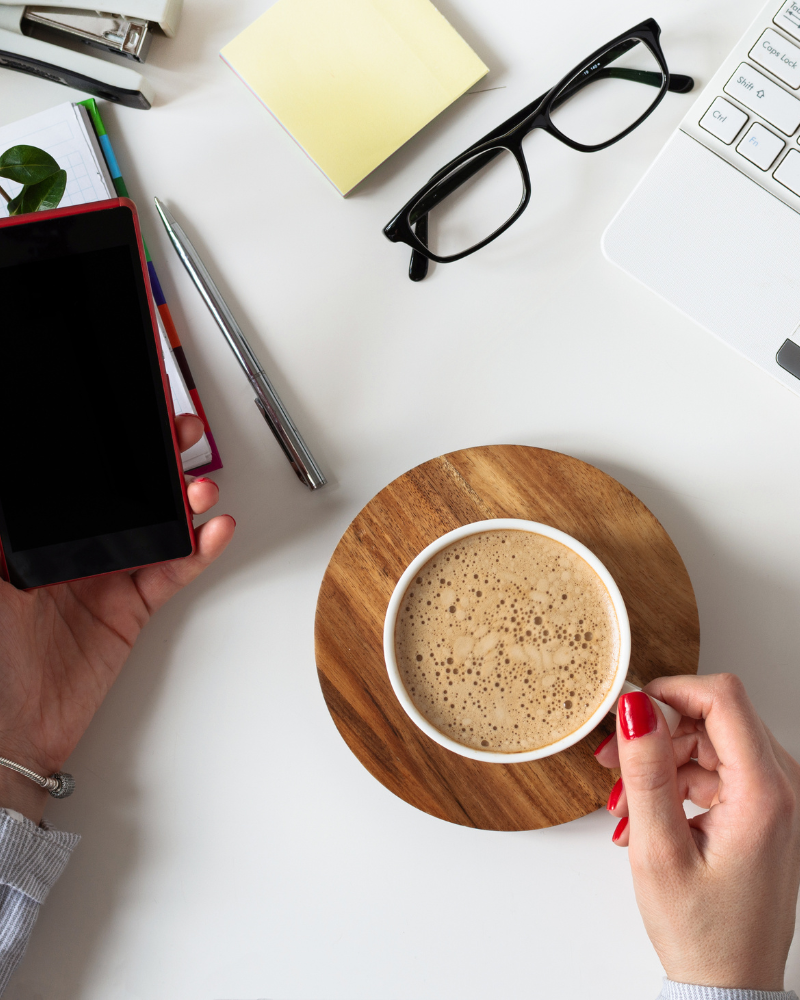 Modern workplace in white desk with woman hand holding mobile phone and a cup of coffee
